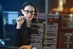 Young bespectacled woman pondering holographic screen, data scientists concept