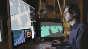 Sustainable emerging technologies concept. Bearded young man working at a computer screen looking at the design of a solar panel array in CAD with data