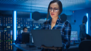 enterprises kubernetes concept. Young bespectacled woman studies laptop in server control room