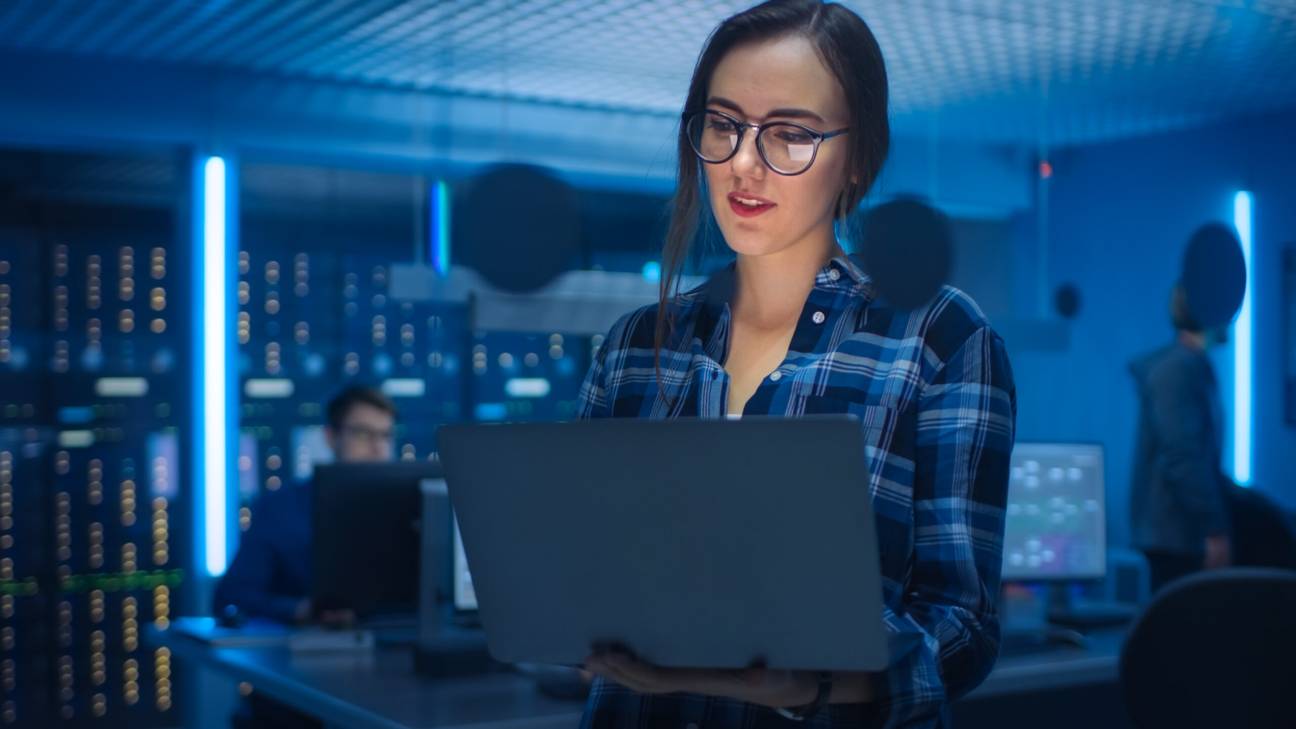 enterprises kubernetes concept. Young bespectacled woman studies laptop in server control room