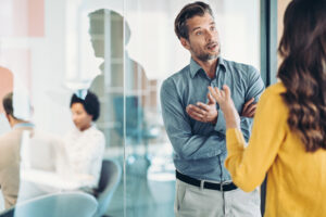 Tech purchasing concept. Bearded man in blue shirt listening to gesticulating woman in yellow top with back to camera